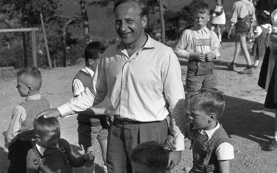 Hermann Gmeiner, grundare av SOS Barnbyar, står utomhus omringad av barn.