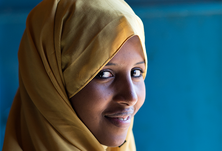 en kvinna med huvudslöja tittar in i kameran och ler.