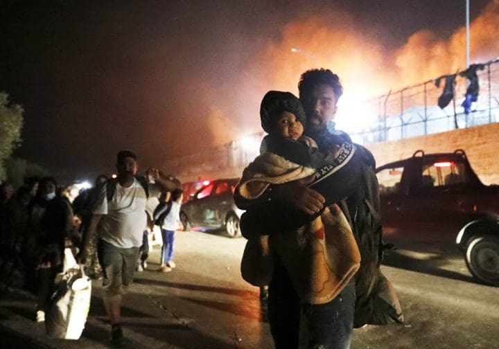 Man som bär på ett barn, det brinner i bakgrunden.