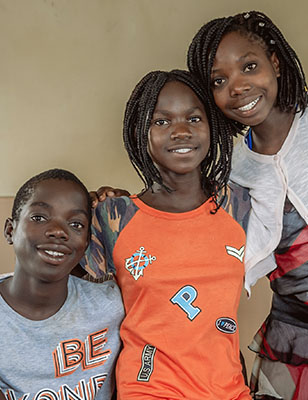 tre ungdomar från SOS barnby ler framför kameran.