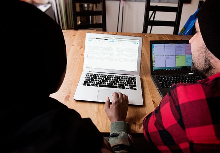 Två personer sitter vid ett bord framför två laptops.