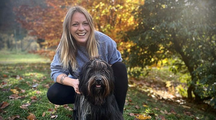 Integrationspedagogen Selma Claesson tillsammans med en svart hund framför höstfärgade lövträd.