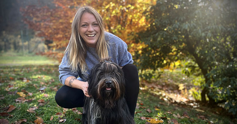 Integrationspedagogen Selma Claesson tillsammans med en svart hund framför höstfärgade lövträd.