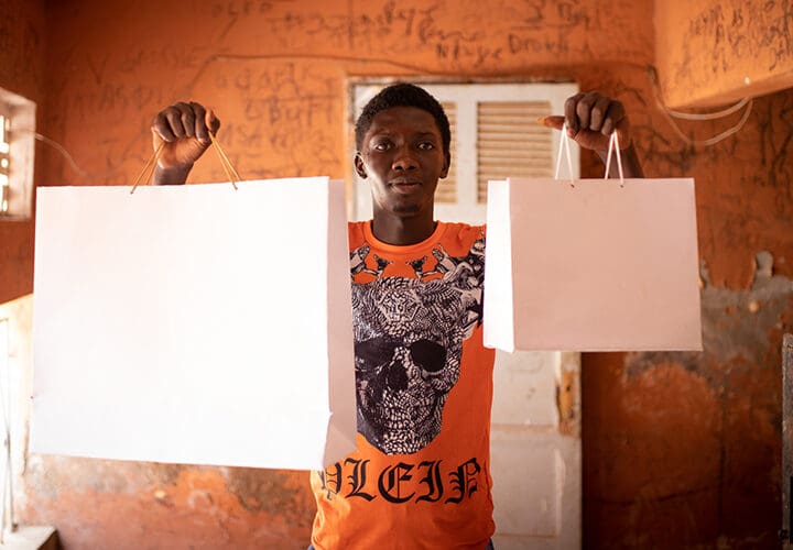 Kille i orange t-shirt med två vita papperspåsar händerna.