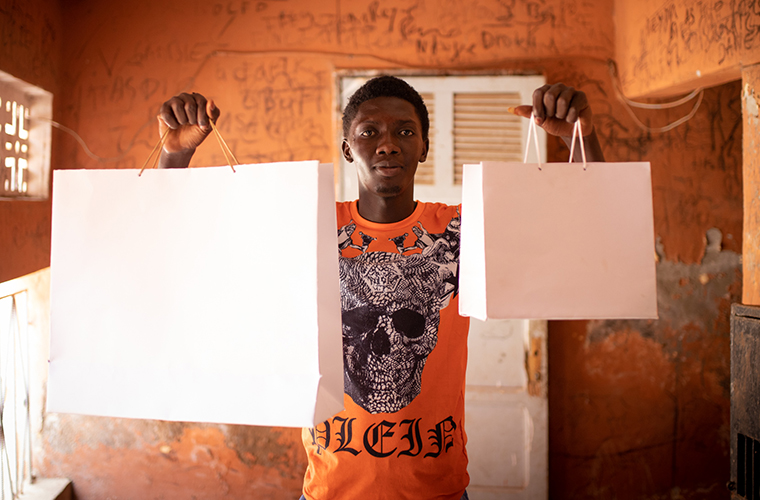 Kille i orange t-shirt med två vita papperspåsar händerna.