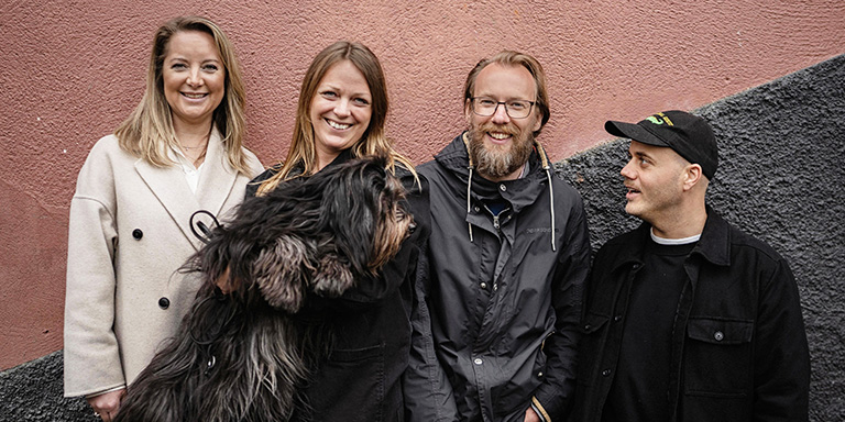 Fyra personer från SOS Barnbyars familjestärkande program, och en hund, står framför en stenvägg.