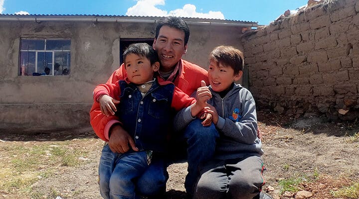 Pappa med sina två pojkar i knät sitter utomhus