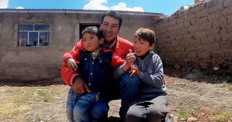 pappa i röd tröja med sina två pojkar i knät sitter utomhus