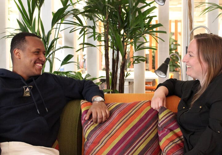 Två personer som sitter i en soffa. De tittar på varandra och skrattar.