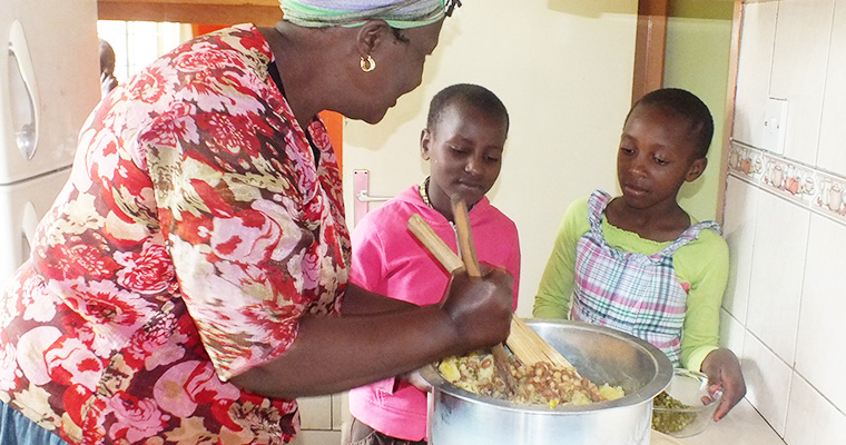 En mamma i blommig skjorta rör i kastrull med två barn