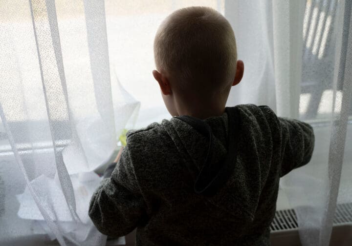 Pojke i motljus tittar ut genom fönstret.