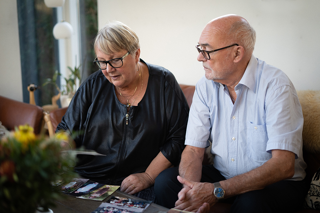 Eli och Flemming som testamenterat till SOS Barnbyar. De sitter i en soffa och tittar på foton av sitt fadderbarn.