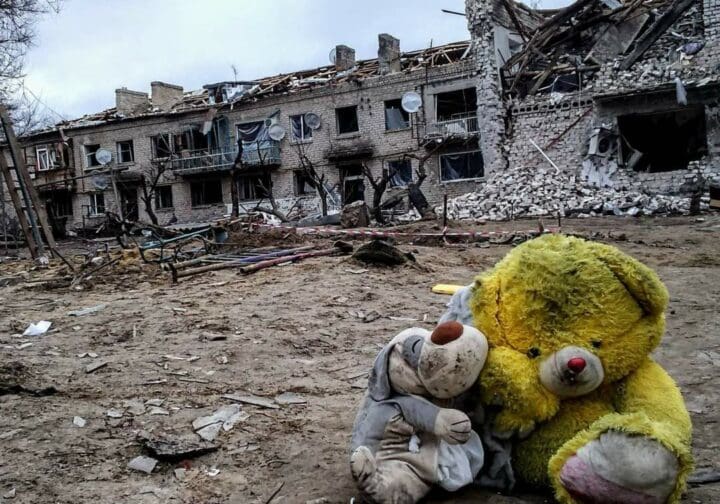 Två gosedjur framför sönderbombade hus i Ukraina.