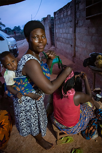 Mamma med barn i sele på ryggen klipper någons hår
