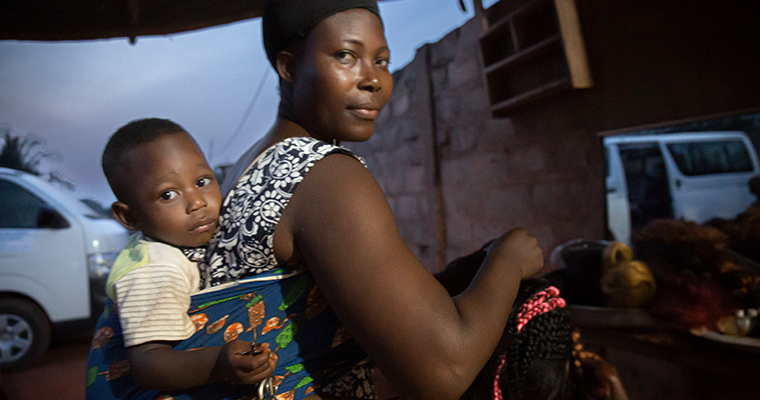 Mamma med ett barn i bärsele på ryggen