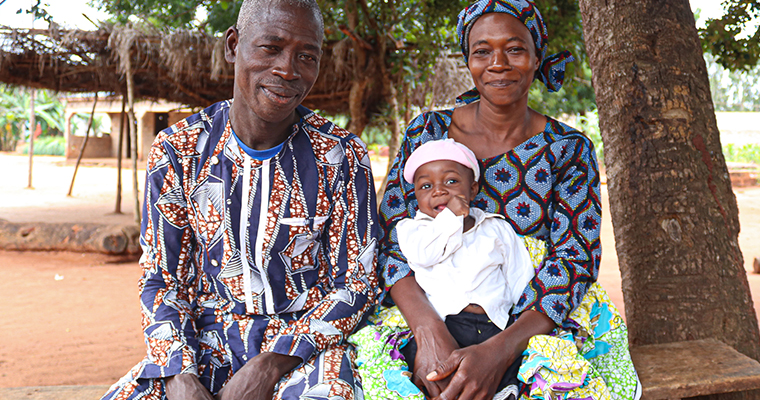 Bebis i vit mössa sitter i mammas knä och pappa bredvid