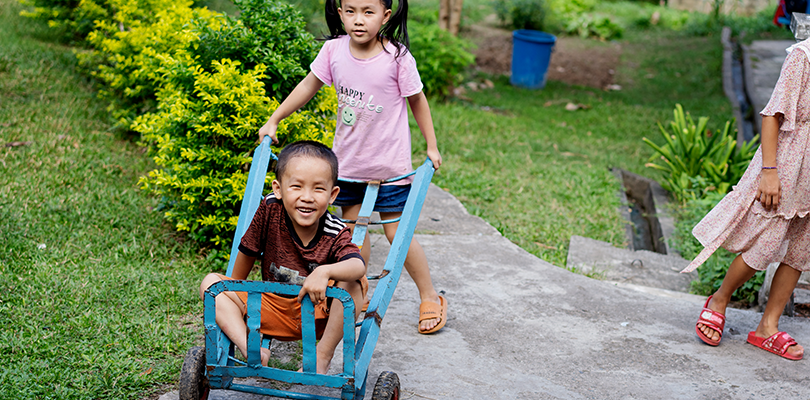 Ett barn kör ett annat barn i en blå liten pirra vagn