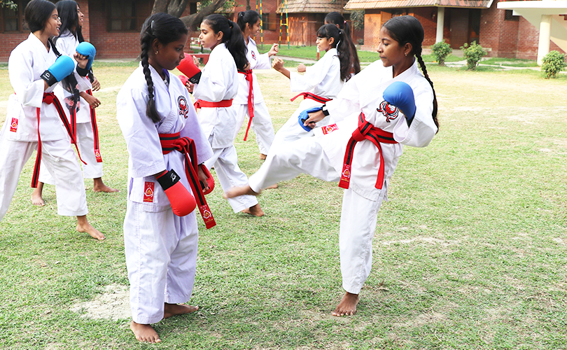 Två flickor i vita kläder och rött skärp på grön gräsmatta utövar karate