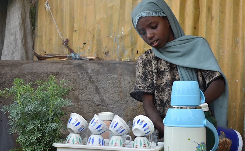 En flicka står bakom ett bord med koppar och säljer kaffe