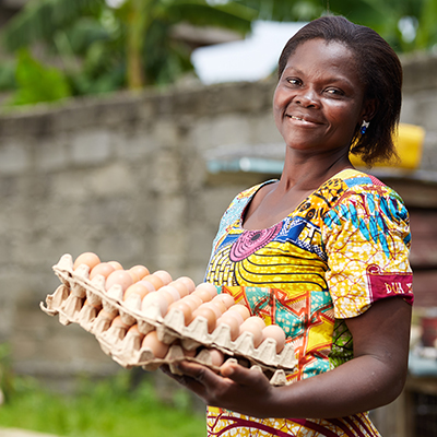 Kvinna i brokig klänning håller äggpaket och ler varmt