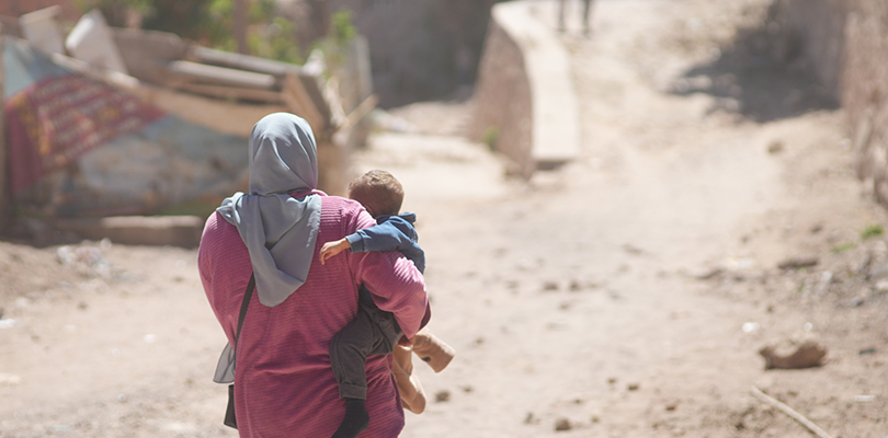 Kvinna syns bakifrån i sjal och bär barn i sina armar 