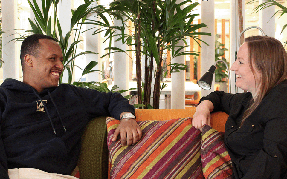 Ungdom och vuxen i SOS Barnbyars ungdomsprogram sitter i en orange soffa och tittar på varandra.