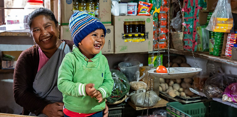 Kvinna i butik skrattar med ett skrattande barn i grön jacka i knät