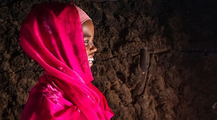 Flicka mot brun vägg i rosa huvudduk i profil skrattar