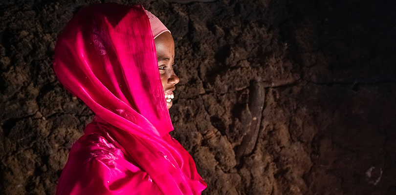 Flicka mot brun vägg i rosa huvudduk i profil skrattar