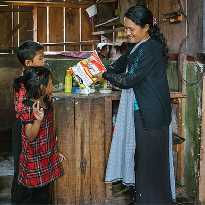 Mamma häller mat i en skål intill två barn