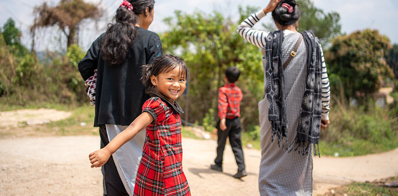 Flicka på en väg håller en kvinna i handen och vänder sig om med glad blick