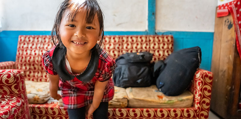 Flicka med busig blick framför en soffa tittar in i kameran