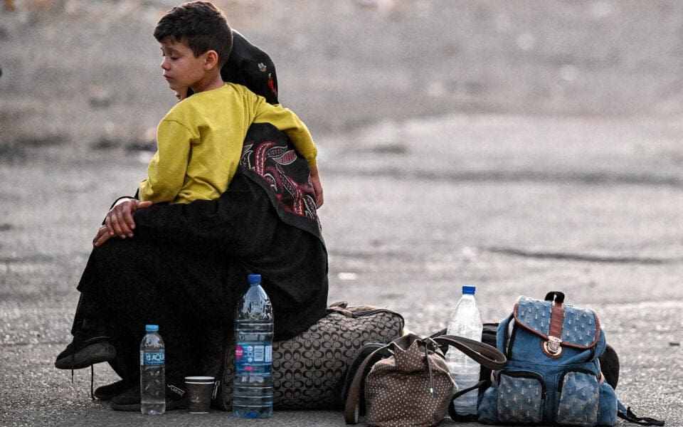 Pojke som sitter i en kvinnas knä bredvid väskor och vattenflaskor.